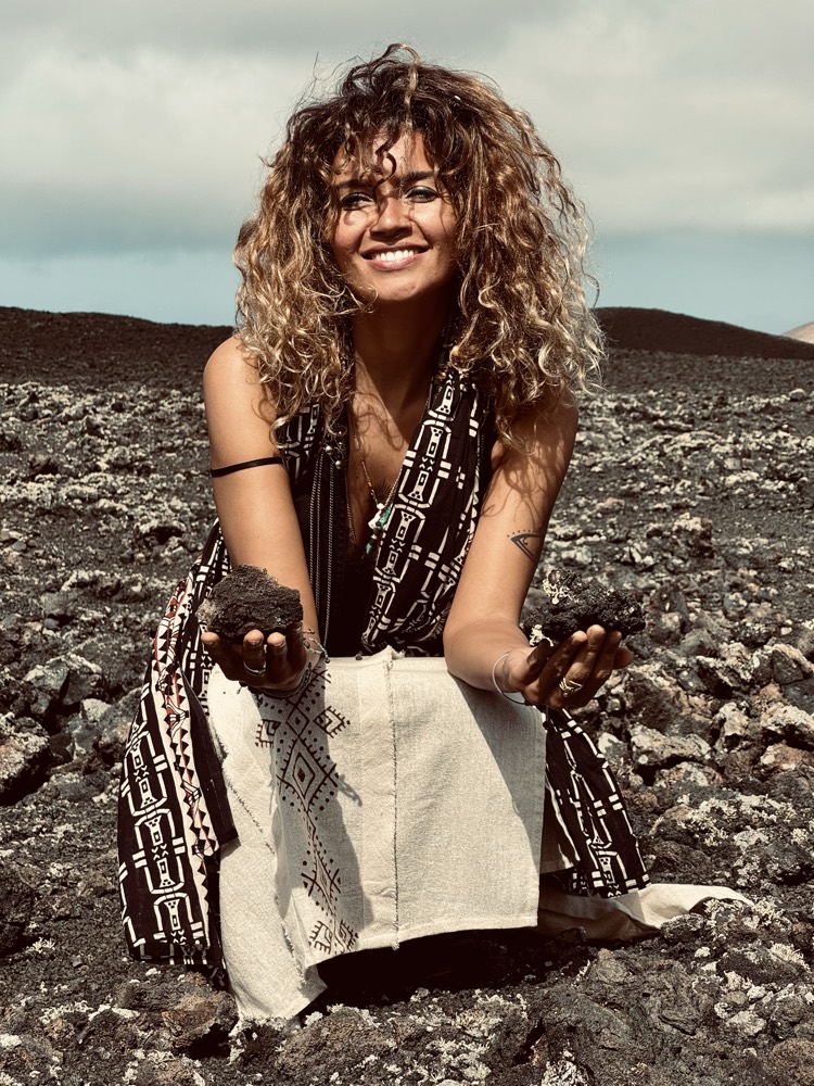 Iana îngenuncheată pe pământ vulcanic, ținând în palme două bucăți de lavă