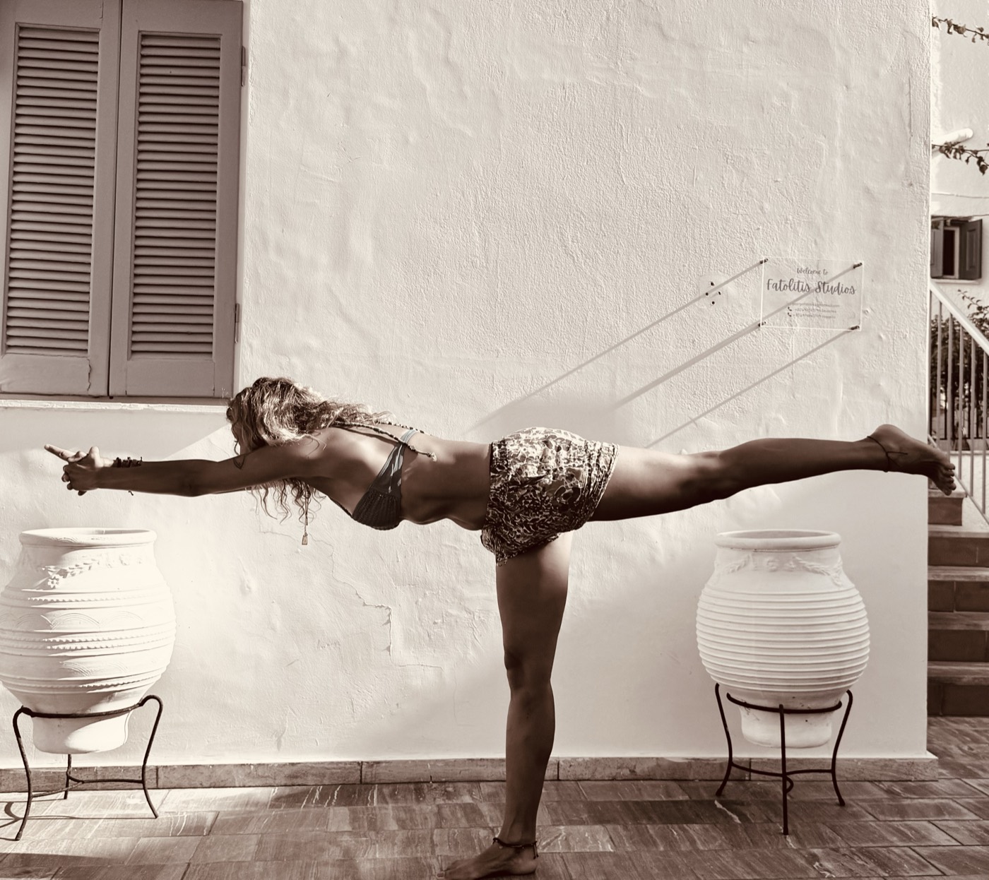 Iana în virabhadrasana III, echilibru pe un picior, lângă un perete alb
